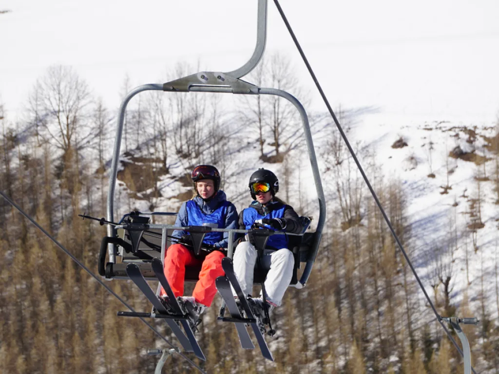 Zwei Jugendliche sitzen im Sessellift über der Piste.